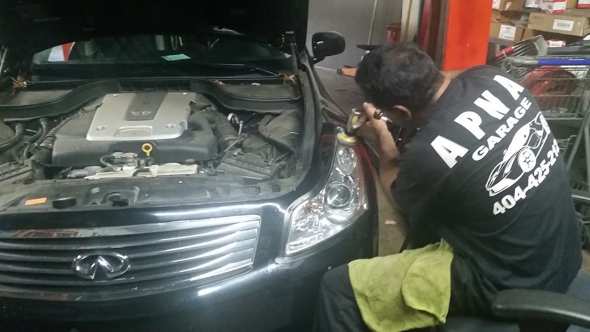 A technician in an Apna Garage shirt working on the front end of an Infiniti