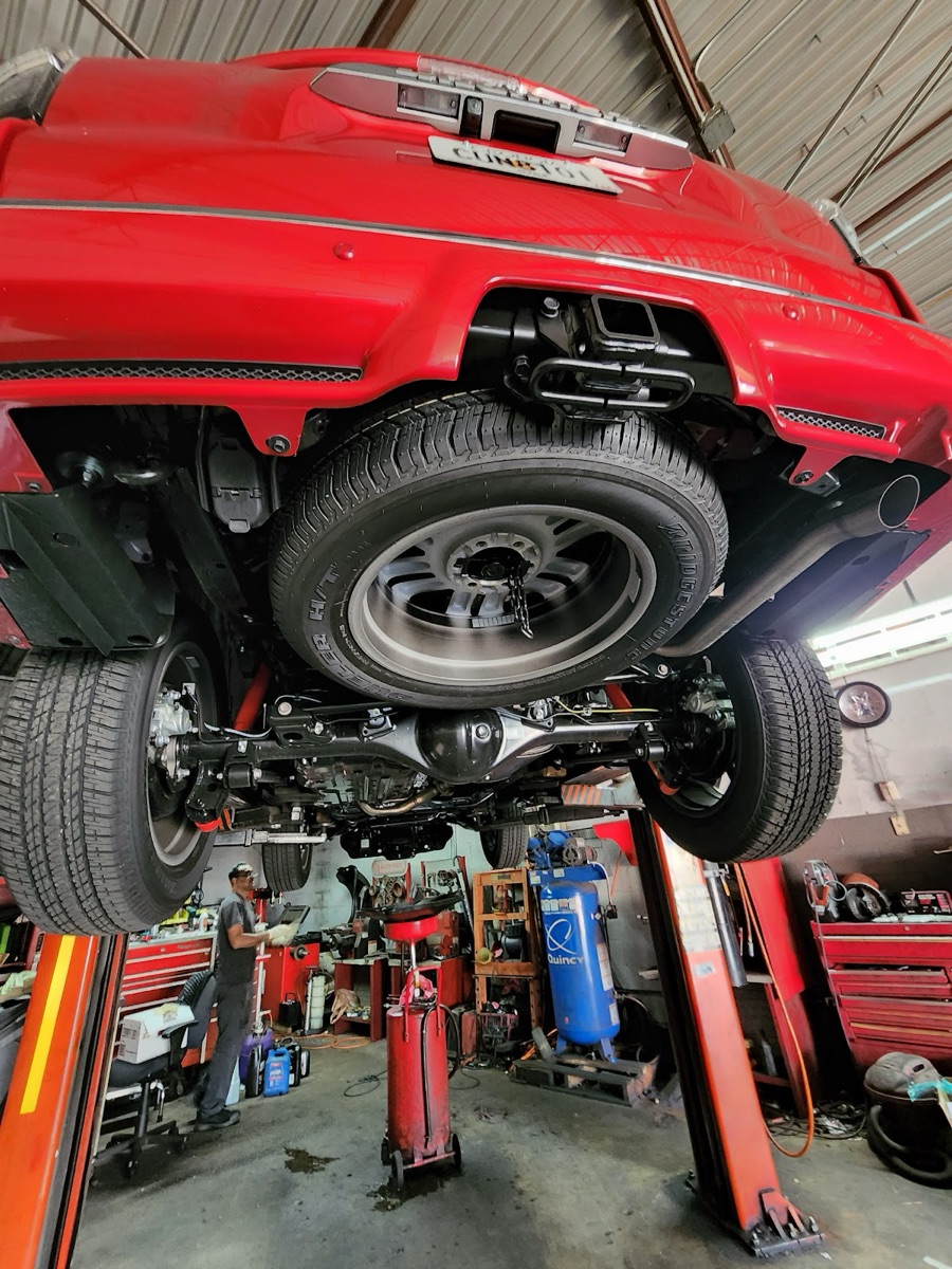 A red SUV raised on the lift for underbody and suspension work at Apna Garage